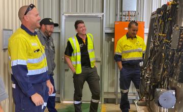 Trades workers standing around a training machine at TAFE laughing together